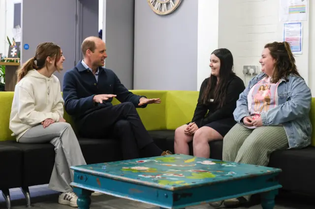 Prince William sits on a couch and speaks with young people from a youth centre in west London