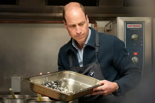 Prince William holding an oven tray with onions in it