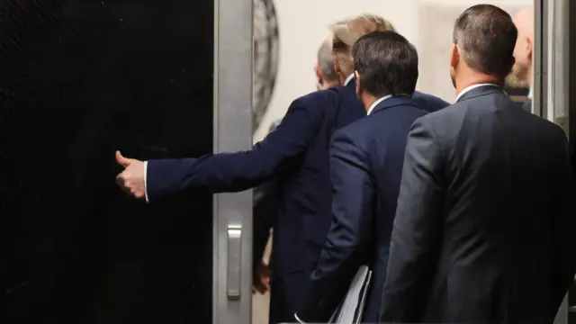 Donald Trump gives a thumbs-up while leaving a courtroom