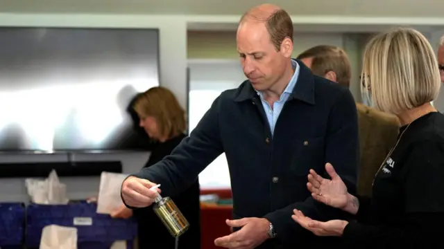 Prince William holding a bottle of an Elemis product, being spoken to by Claire Hopkins