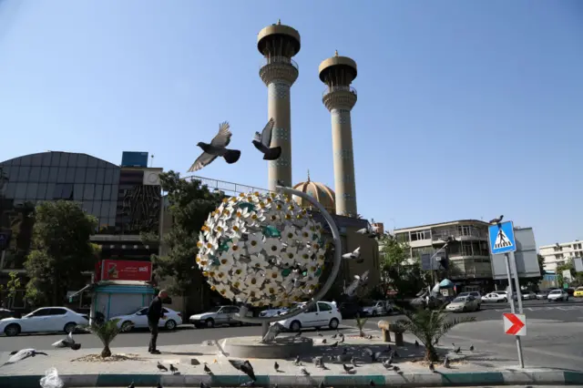 Man feeds the pigeons by a sculpture in Tehran