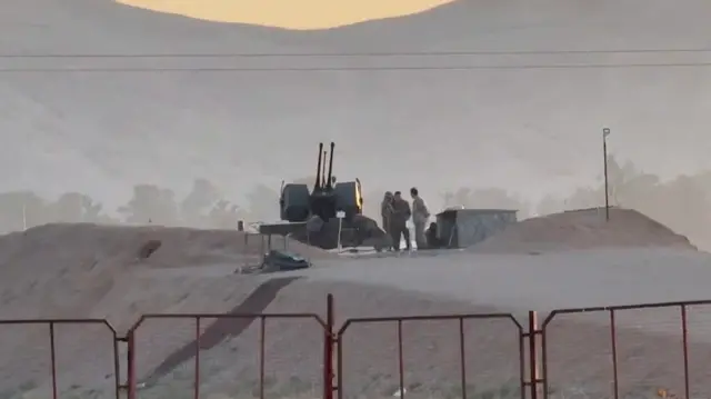 Military personnel stand near equipment