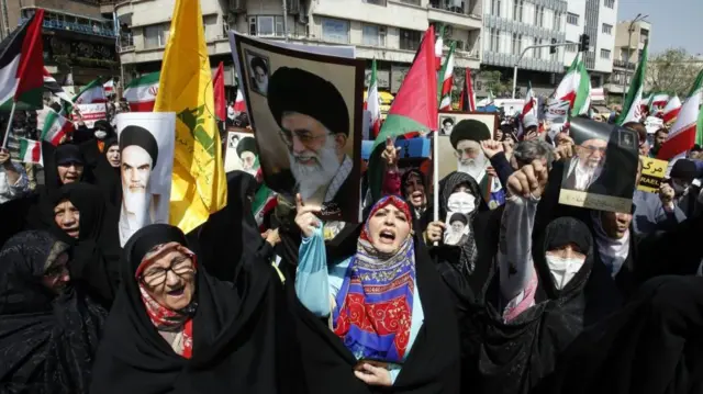 Women in Hijab hold portraits of former Iranian leaders and carry flags at the rally in Tehran