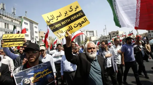 A group of men at the protest, one is holding a sign which reads "Down with Israel" in English, Persian and Arabic.