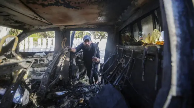 A man looks into a burnt out car in Deir al -balah