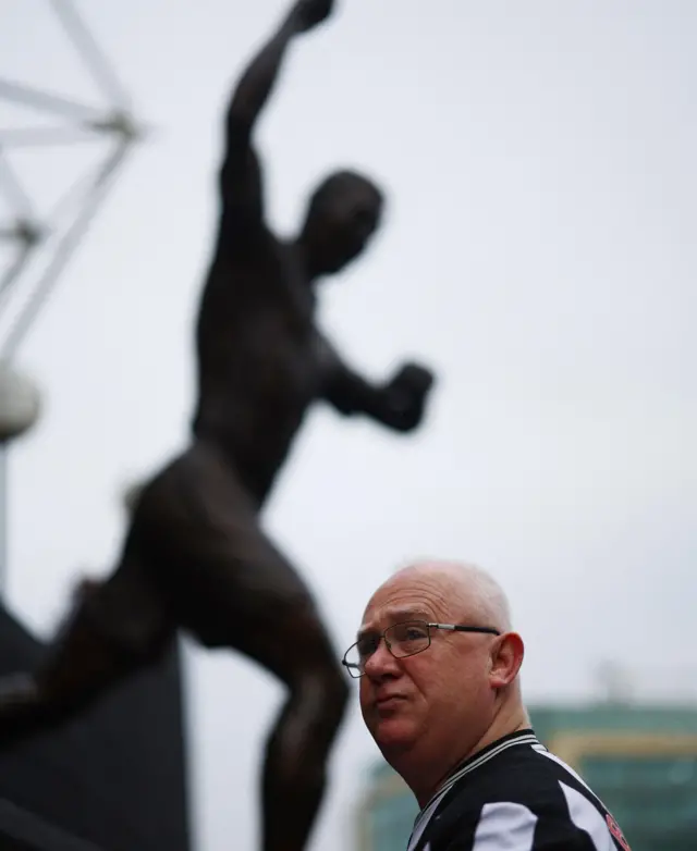 A Newcastle fan stands in front of the Alan Shearer statue at SJP/