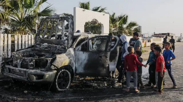 Children crowd round a burnt-out car in Deir al-Balah