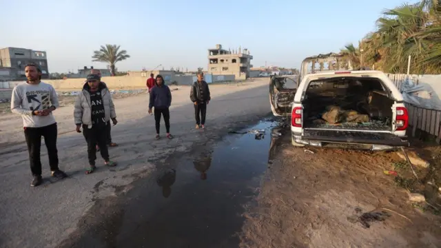 Palestinians stand next to a vehicle where employees from the World Central Kitchen (WCK) were killed.