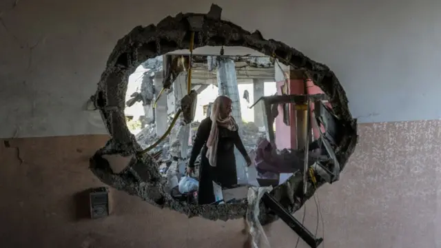 A woman is seen through a massive hole in the wall of a home hit by strikes in Rafah