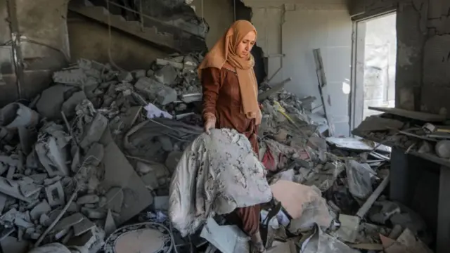 A woman examines the destroyed and damaged buildings and the damaged area around them collect remaining belongings from the rubble of heavily damaged buildings in the east of Rafah, Gaza