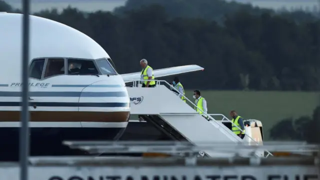 Members of the staff in green reflective vests board a plane reported by British media to be first to attempt to transport migrants to Rwanda