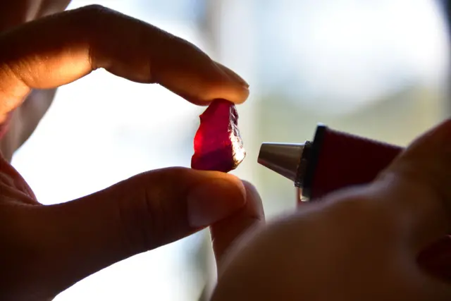 A worker examines a large ruby at a mine in Mozambique. Stock photo.