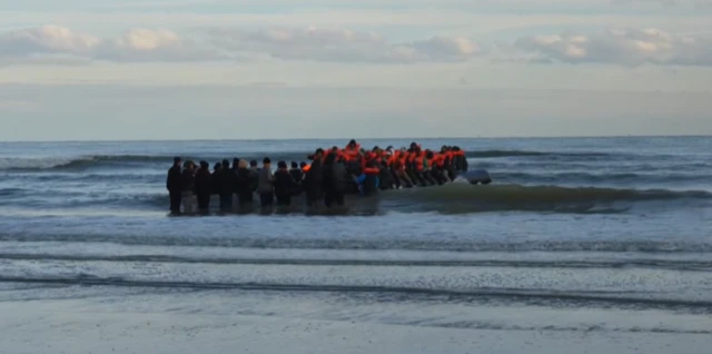 A small dinghy crammed with people wearing life vests arrived on the shore near Calais