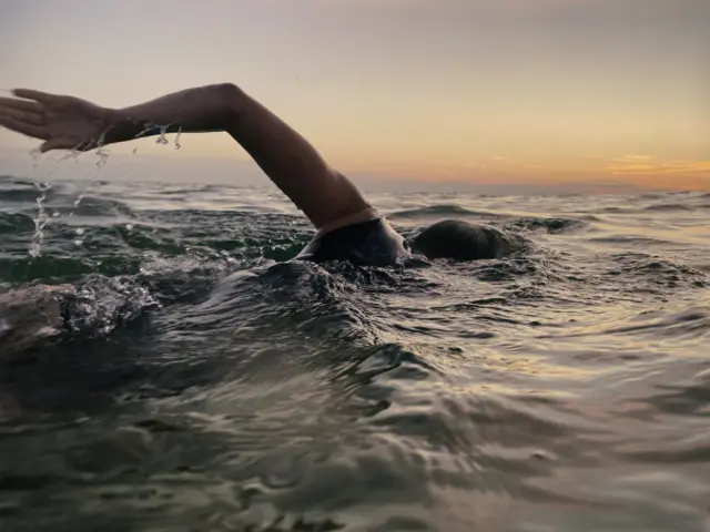 Woman swims in sea at sunset