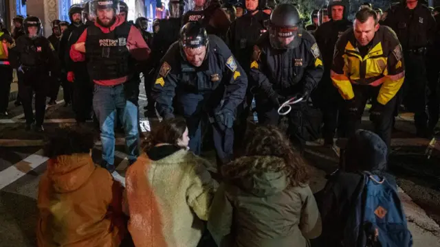 Police confront a row of protesters seated on the ground in Boston