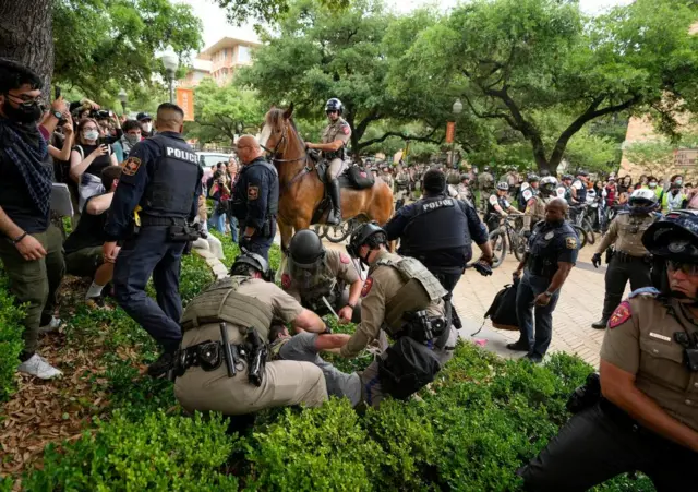 Chaos as police and protesters mix. A protester is pushed into a bush by several police officers