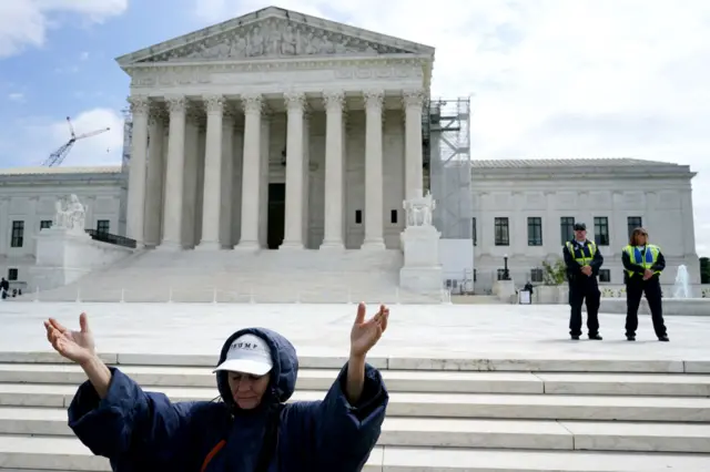 A trump supporter seeming to pray outside the Supreme Court, while police watch on.