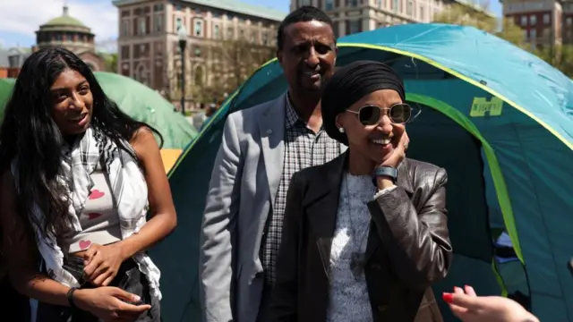 Ilhan Omar smiles as she speaks with students near green tents