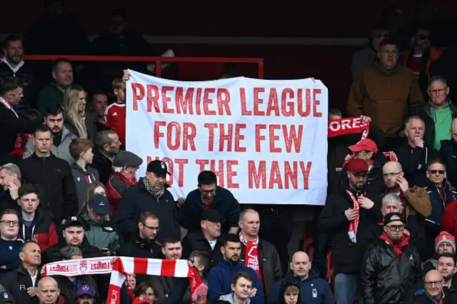 A fan holds a banner reading 'Premier League for the few not the many'