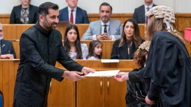 Humza Yousaf handing over a document in a courtroom as he becomes first minister in 2023