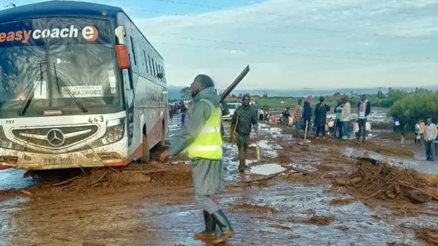 A man in a reflective shirt stands in water next to a bus in the road