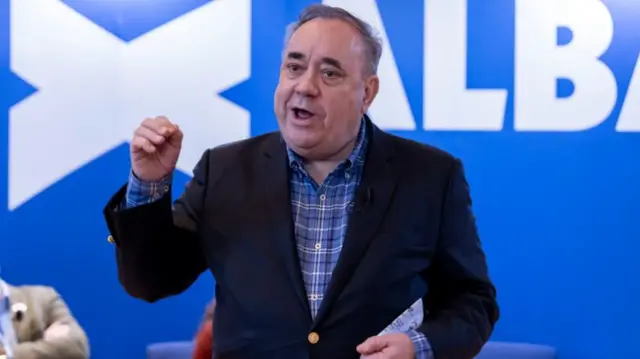 Alex Salmond speaking in front of a blue and white Alba party banner