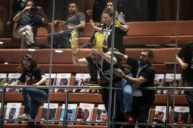 Man smearing yellow paint on glass above the plenum as part of a demonstration at the Knesset