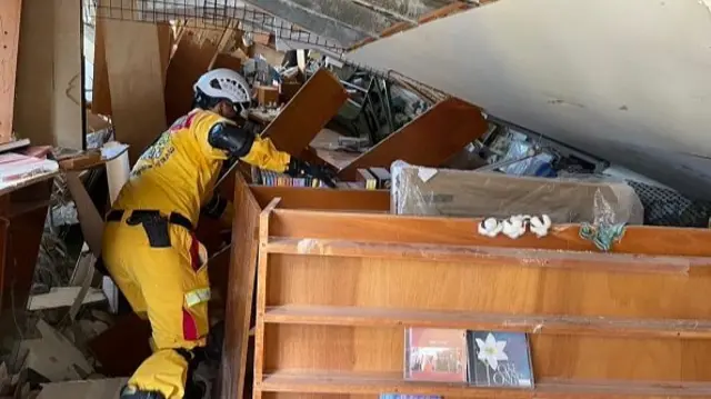 A rescue worker searches inside a building where shelves have fallen on each other