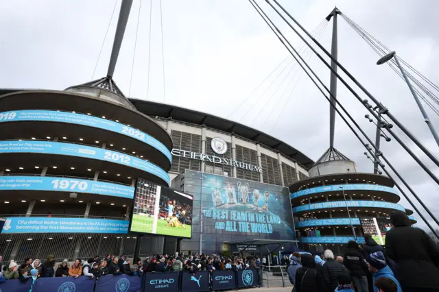 Fans stand outside the Etihad stadium waiting for the bus to arrive