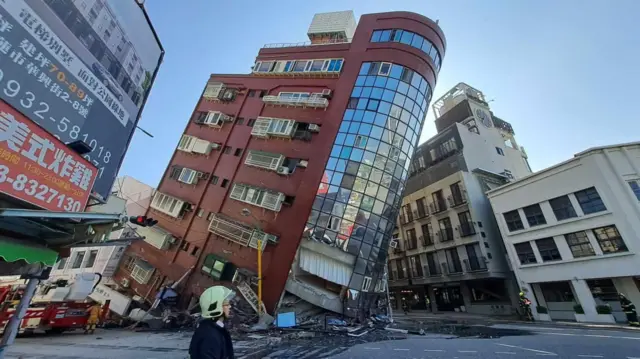 A red building with a glass front leans dangerously