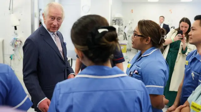 Charles speaks to two female nurses in blue scrubs