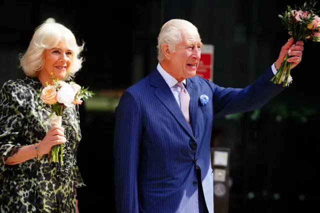 King Charles III and Queen Camilla wave to members of the public as they hold flowers in their hands