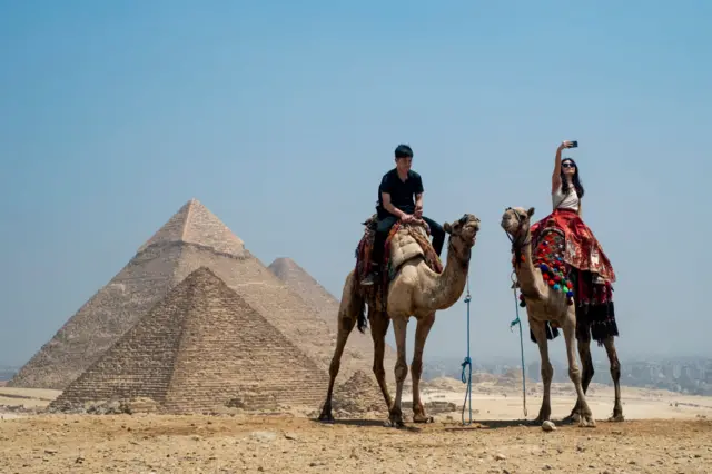 A tourist takes a selfie while riding a camel at the Giza Pyramids Necropolis on the outskirts of Giza on April 30, 2024.