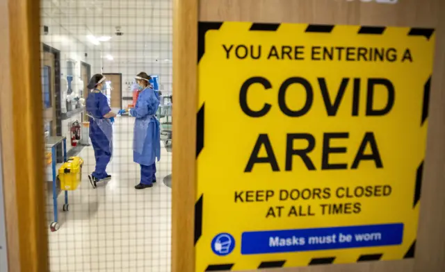 Covid-19 warning sign on door, medical staff in PPE