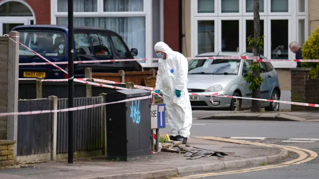 Forensic investigator standing by a street sign within the cordon