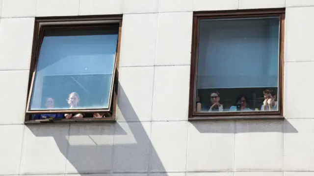 People look out two windows in a concrete building, many with their phones propped against the glass