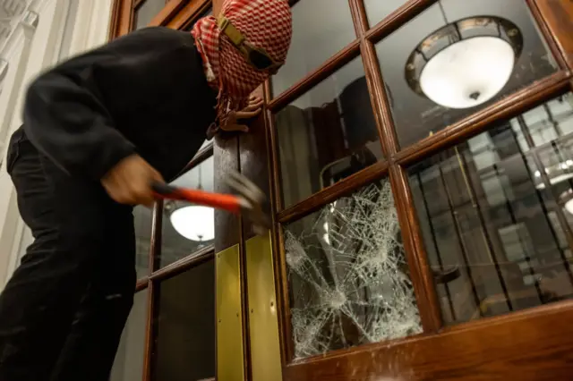 A protester uses a hammer to smash their way into Hamilton Hall