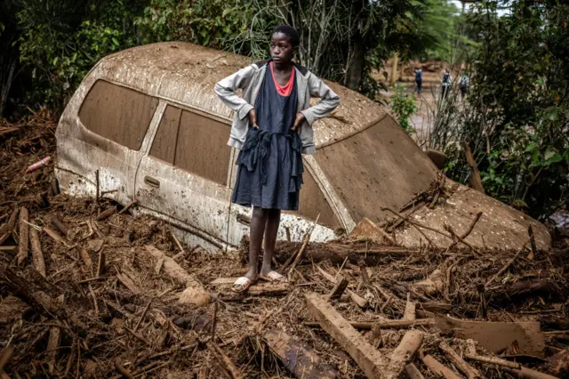 A girl looks on next to a damaged car buried in mud in an area heavily affected by torrential rains and flash floods in the village of Kamuchiri, near Mai Mahiu, on April 29, 2024. At least 45 people died when a dam burst its banks near a town in Kenya's Rift Valley, police said on April 29, 2024