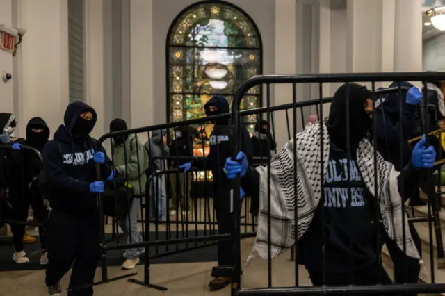 Students with their faces covered carry metal barriers