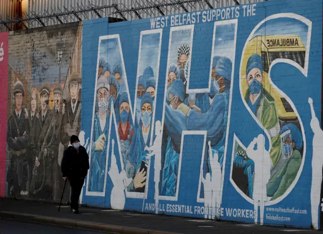 Person wearing mask walking past a mural depicting NHS workers