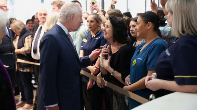 Charles speaks to a woman in a crowd. She holds her hands to her chest and smiles back at him.