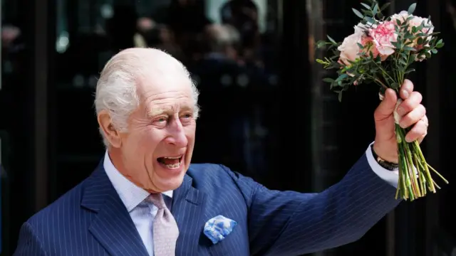 The King raises a bouquet of flowers into the air, smiling