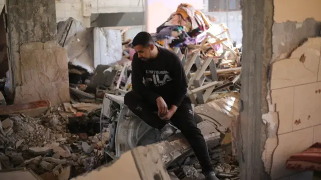 A Palestinian man perches on a pile of rubble inside a destroyed Rafah house, staring at the ground