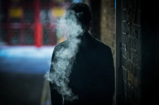 Silhouette of a man, engulfed in smoke, photographed from behind in a dark alleyway