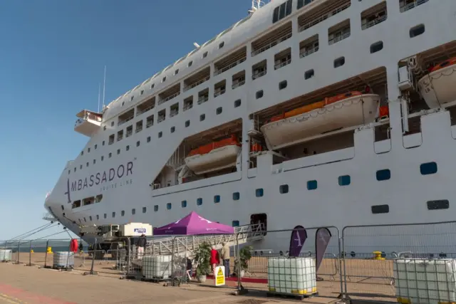 Invergordon, Scotland, UK, Cromarty Firth port security fence and cruise ship alongside with welcome tent for disembarking passengers against a blue sky.