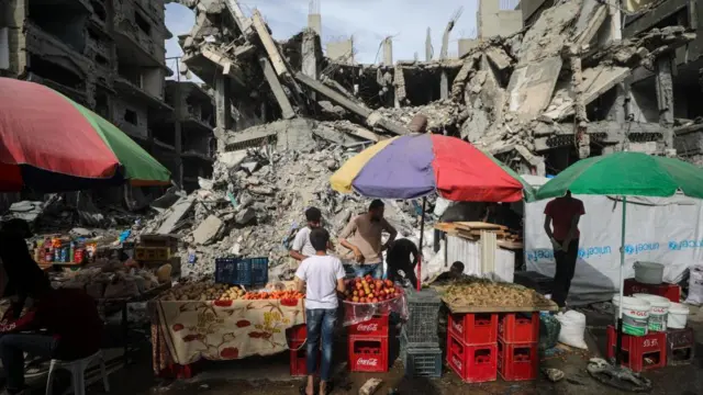 Palestinians walk past kiosks set up next to destroyed buildings on the last Friday of Ramadan along a street in Al Nusairat refugee camp, Gaza Strip, 05 April 2024