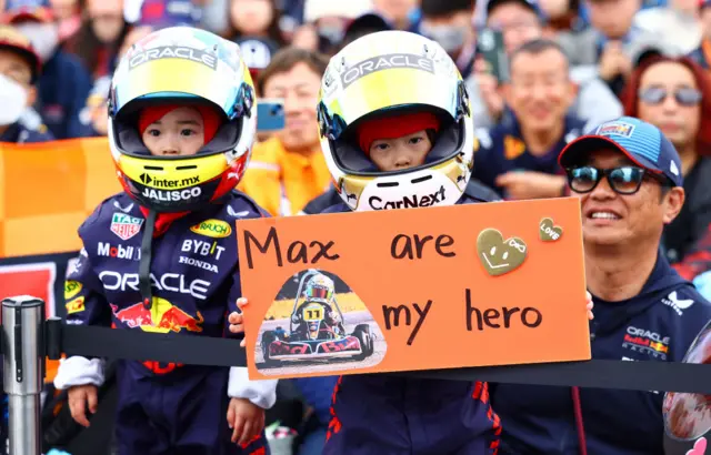 Two young Max Verstappen Verstappen fans wear full race suits and hold up signs