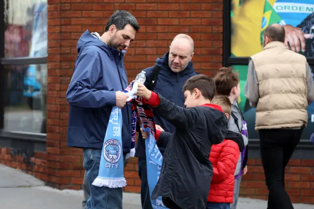 A fan holds up a half and half scarf after purchasing outside the ground