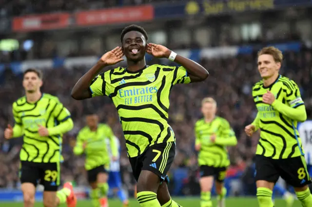 Saka cups his ears and sticks out his tongue as he celebrates his goal