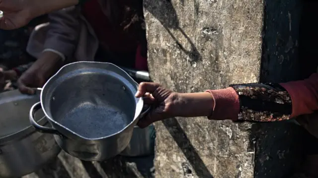 A displaced Palestinian child holds up an empty pot as she waits with others to receive food aid provided by a Palestinian youth group in the Rafah refugee camp, Southern Gaza Strip, 25 January 2024